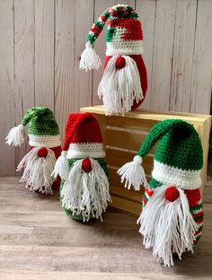 three knitted christmas gnomes sitting on top of a wooden box next to each other