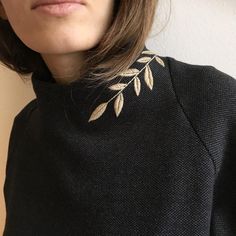 a close up of a person wearing a black sweater with gold leaves on the collar