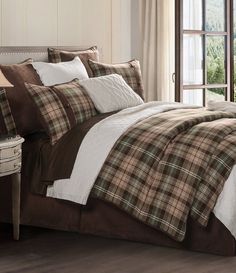 a bed with plaid comforter and pillows in a room next to a large window