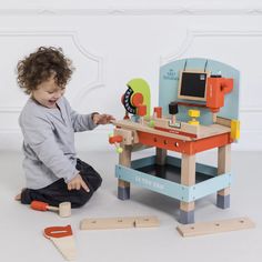 a toddler playing with a wooden toy computer desk and matching toys on the floor