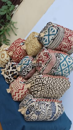 several pillows are stacked on top of each other in different colors and patterns, along with a blue table cloth