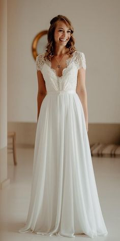 a woman in a white dress is smiling at the camera while standing next to a mirror