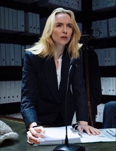 a woman sitting at a table with a microphone in front of her and papers on the desk