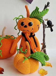 an orange crocheted stuffed animal sitting on top of a pumpkin next to a tree