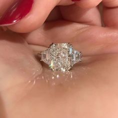 a woman's hand holding an engagement ring with three stone diamonds on the side