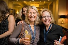 two women are smiling and holding drinks in their hands