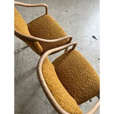 two wooden chairs sitting on top of a cement floor next to each other and one has a yellow seat cushion