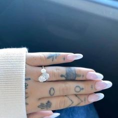 a woman's hand with tattoos and a diamond ring on her left thumb, in the background is a car