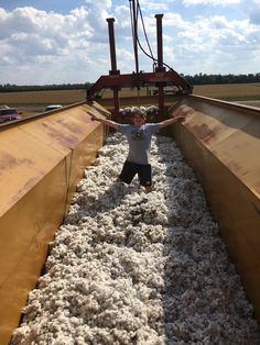 a young boy standing in the middle of a pile of white wool next to a machine