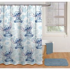 a blue shower curtain with lil the stitcher and flowers on it, in front of a window