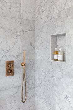 a bathroom with marble walls and flooring, including a gold shower faucet