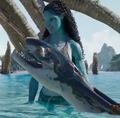 a woman is holding a dolphin in the water with palm trees around her and another creature behind her