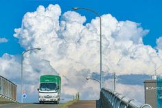 a green and white bus driving over a bridge under a cloudy blue sky with clouds