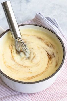 a whisk in a white bowl on top of a red and white checkered cloth