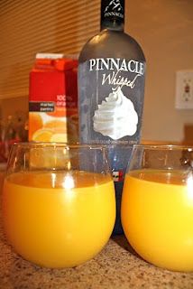 two glasses filled with orange juice sitting on top of a counter next to a bottle