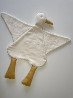 a white and yellow duck shaped cloth toy on a white surface with one wing extended