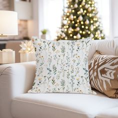 a living room with a christmas tree in the background and pillows on the couches