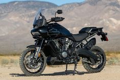 a black motorcycle parked on top of a dirt road in front of some mountains and hills