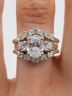 a woman's hand holding a ring with three stones on it and the center stone is surrounded by smaller round diamonds