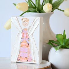 a white vase filled with flowers and a paper cutout of a woman in a pink dress