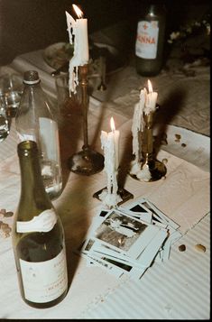 a bottle of wine sitting on top of a table next to some candles and pictures