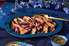 a blue platter filled with meat and vegetables on a table next to wine glasses