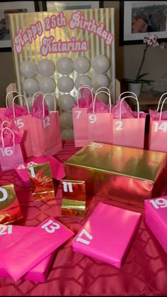 pink and gold gift bags with numbers on them sitting on a red tablecloth in front of balloons