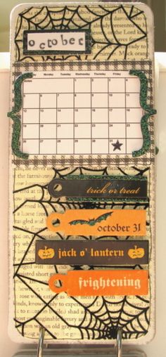 a desk calendar with spider webs and pumpkins on the front, attached to a metal holder