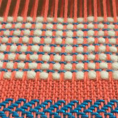 an orange, blue and white weaving pattern on a piece of cloth with some thread