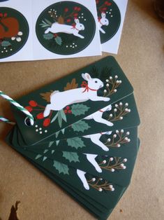 four green christmas cards with white rabbits and holly wreaths on them, sitting next to each other