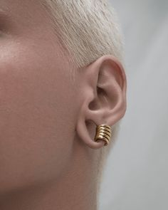 a woman with white hair wearing gold earring in the shape of a spiral design