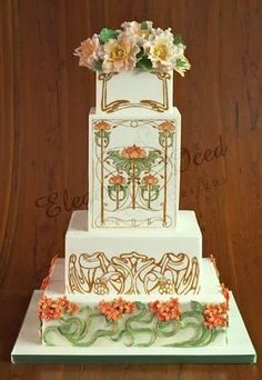 a three tiered cake decorated with flowers and vines on a wooden table next to a wall