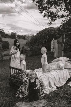 three women and two children standing in front of a bed with clothes hanging on the clothesline