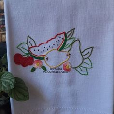 a white towel with embroidered fish and watermelon design on it next to a potted plant