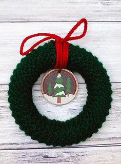 a christmas wreath ornament hanging from a red ribbon on a white wooden background