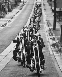 a group of people riding on the back of motorcycles down a street in black and white