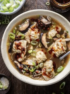 a bowl filled with dumplings and vegetables on top of a wooden table next to other bowls