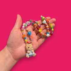 a hand holding a small beaded teddy bear necklace on it's wrist,