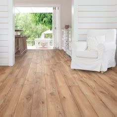 a living room with white furniture and wood flooring on the walls, along with an open door leading to a porch