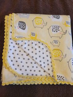 a yellow blanket with elephants on it and polka dot trim around the edges, sitting on a brown surface