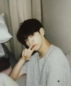 a young man sitting on top of a bed next to a pillow covered in white sheets