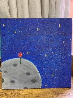 a painting on a wooden table with a red flower in the sky and stars above it