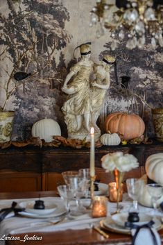 the table is set with plates, candles and pumpkins in front of a wallpapered background