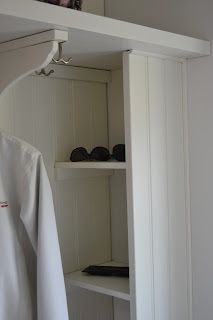 an open closet with white clothes hanging from the ceiling and shoes on shelves in front of it