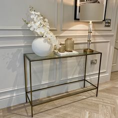 a glass table with flowers on top and a lamp next to it in a room