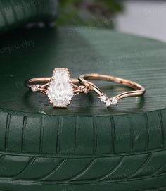 two wedding rings on top of a green car tire, one with an oval cut diamond and the other with three smaller round diamonds