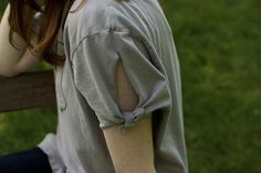 a woman sitting on a wooden bench with her arm wrapped around the back of her shoulder