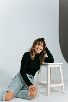 a smiling woman sitting on the ground in front of a stool and posing for a photo