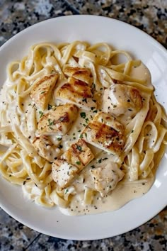 a white plate topped with pasta covered in sauce and chicken breast pieces on top of it