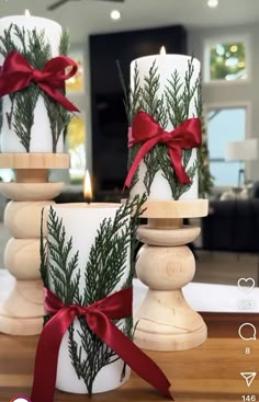 two white candles with red bows and pine branches on them, sitting next to each other